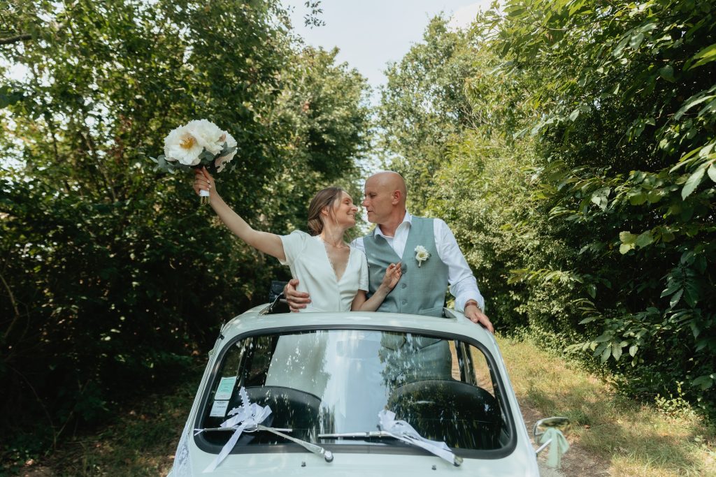 Les mariés sortent de la capote de la voiture les mains en l’air