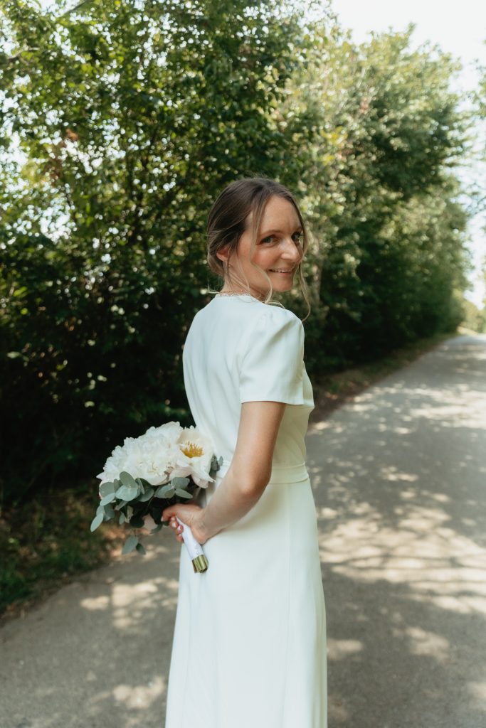 La mariée en portrait qui tient son bouquet de fleurs dans son dos